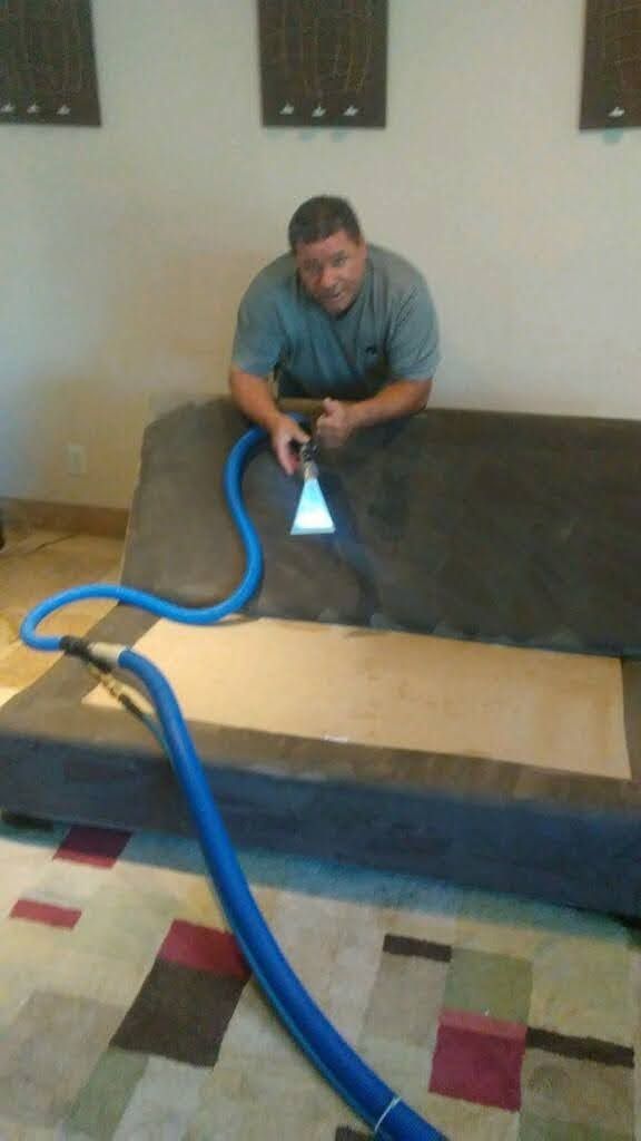 A man cleaning a couch cushion with an upholstery tool