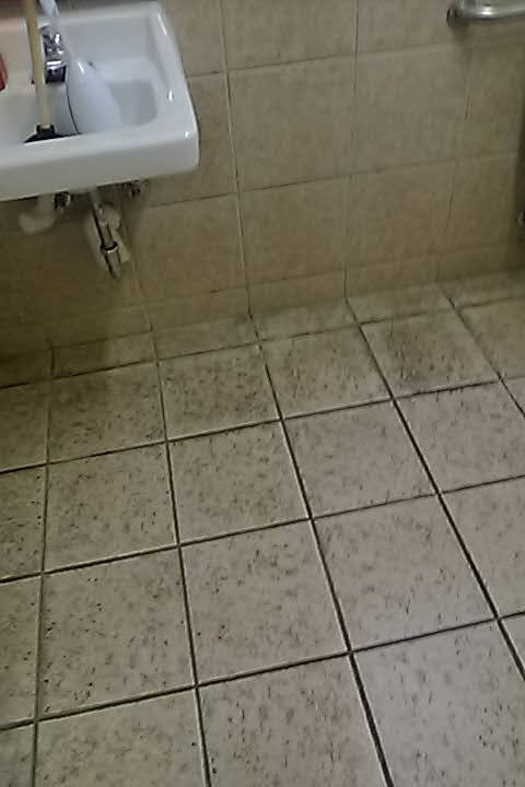 A dirty tile floor with dark speckled grout lines beneath a sink