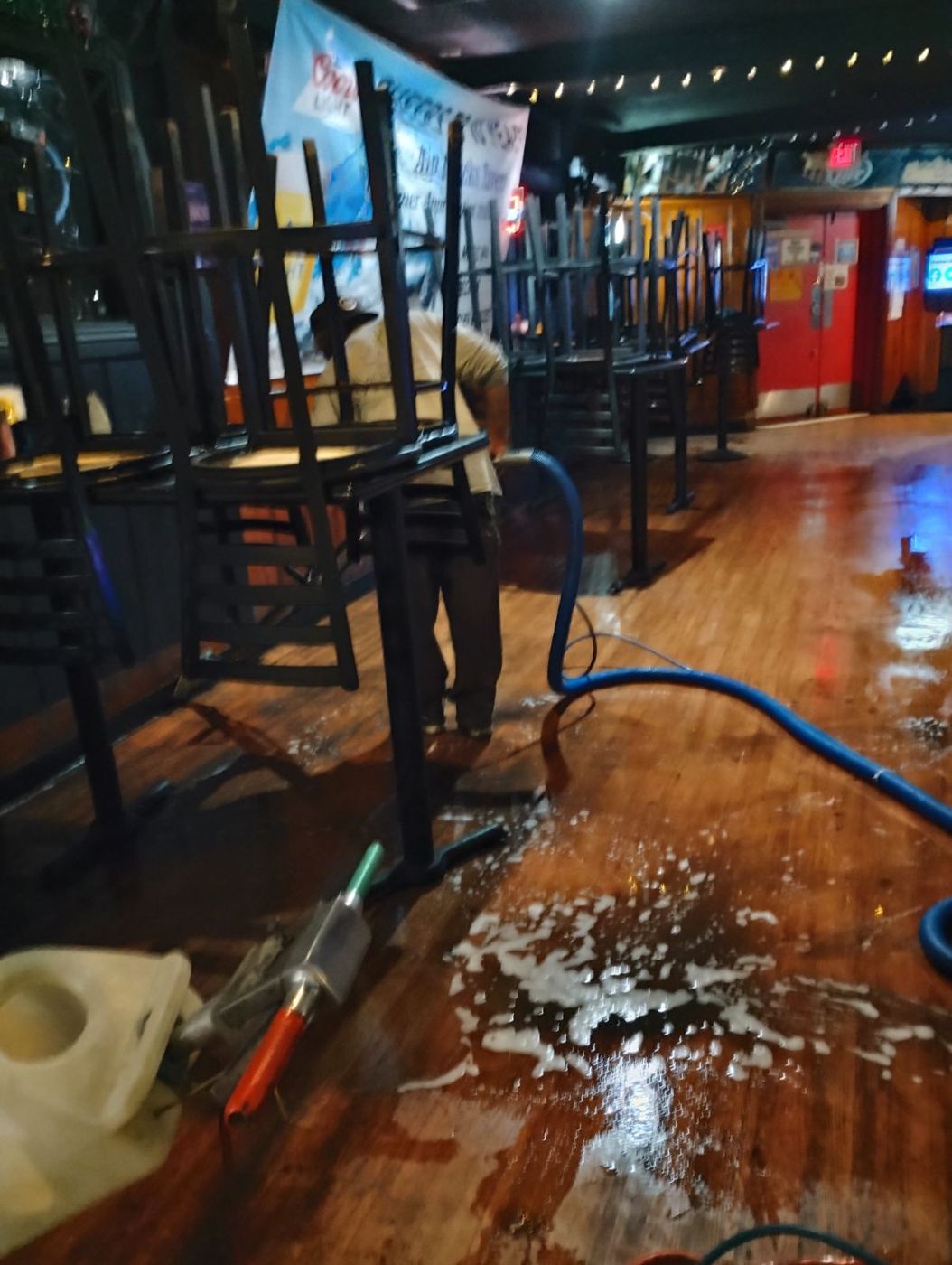 A technician cleaning a restaurant floor with chairs stacked on the tables