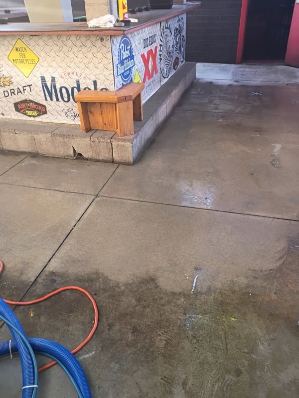 A bar patio's concrete being cleaned, with the clean section beside the dirty one